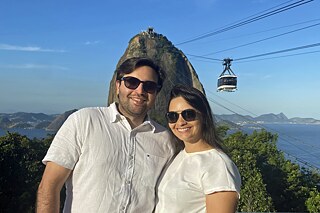 Zwei Personen in weißen Oberteilen stehen zusammen, im Hintergrund fährt eine Seilbahn zum Zuckerhut