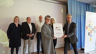 Sechs Personen bei Verleihung der PASCH-Plakette in Innenraum