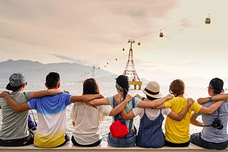 Jugendliche sithen auf einer Kaimauer; sie legen sich gegegnseitig die Arme über die Schultern und blicken in die Ferne.