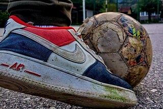 Ein Sportschuh an einem Fussball auf einem Sportplatz.