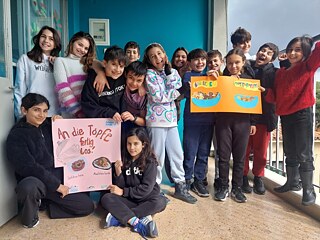 Gruppenfoto von der jüngsten teilnehmende Schulklasse. Die Schülerinnen und Schüler halten selbst gemachte Plakate in die Kamera. 